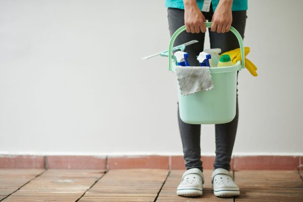 Close-up of cleaning worker holding bucket with different supplies for housework