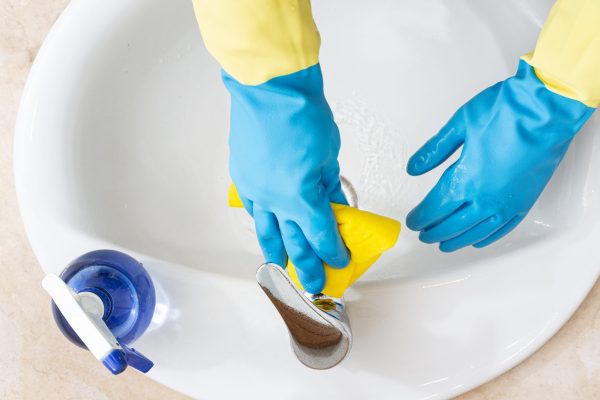 Hands with gloves cleaning a bathroom with a yellow rag. Disinfection or hygiene concept