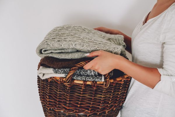 Stack of knitted sweaters on the wicker basket in young female hands